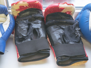 closeup of worn out one pair boxer gloves in fight club, red and black peeled leather