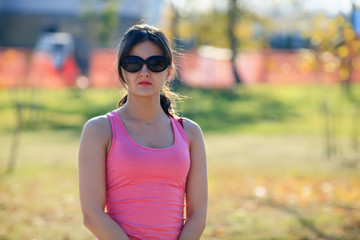 Portrait of a young cute girl in sunglasses and a pink t-shirt in the park on an autumn day.