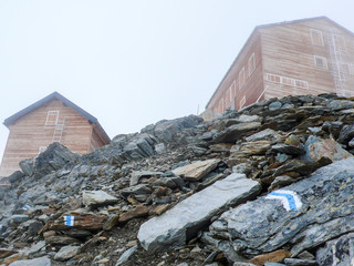 Poster - two wooden mountain huts high up in the Alps of Switzerland on a cloudy and foggy day 