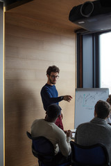 Canvas Print - Young caucasian sales manager presenting new project to his multiethnic colleagues, reporting about work result with flipchart.