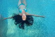 schöne reife Frau im besten Alter mit dunklen Locken im blauen Bikini im Sonnenlicht schwebt schwerelos elegant glücklich schwimmend in türkis blauem Wasser im Wellness Pool