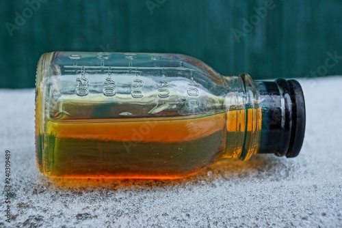 Fotografía brown liquid from machine oil in a glass bottle on white snow on a green backgro