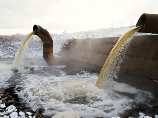 wastewater from two large rusty pipes merge into the river in clouds of steam