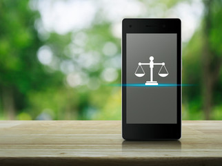 Law flat icon on modern smart mobile phone screen on wooden table over blur green tree in park, Business legal service online concept