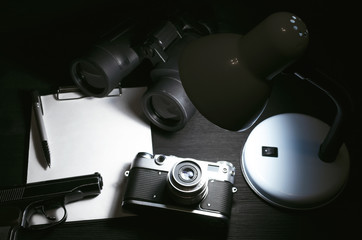 Wall Mural - blank page, pen, film photo camera, handgun and a binoculars on a black detective agent table backgr