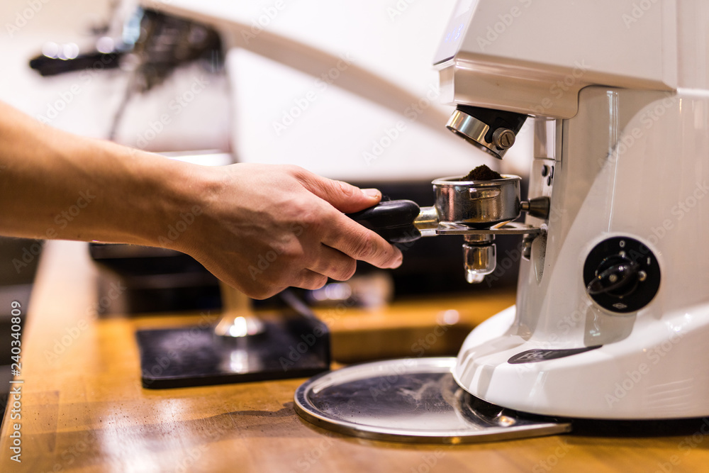 Barista grinding coffee beans using coffee machine, coffee grinder grinding freshly roasted make beans into a powder.