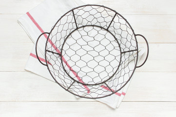 Metal wire empty Bowl Sieve and kitchen towel on rustic white wooden background top view flat lay copy space. Table setting, kitchenware, single item, cooking items.