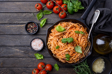 Spaghetti pasta with tomato sauce and basil over wooden background, top view