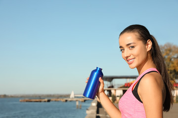 Wall Mural - Young sporty woman with water bottle outdoors on sunny day. Space for text