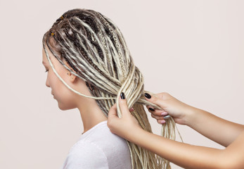 A hairdresser weaves dreadlocks to a beautiful young girl in a hairdresser's.