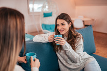 Two Young Female Friends Drinking Tea While Sitting On The Sofa At Home.