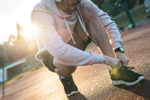 Fotografía Young sportsman tying shoelace while crouching and listening to music in the mor