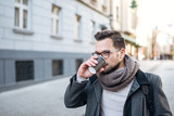 Fototapeta Miasto - Close-up image of young man walking and drinking coffee in the city street.