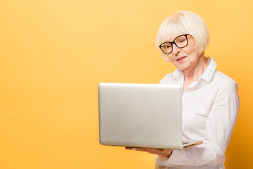 Senior business woman with laptop. Isolated over yellow background.