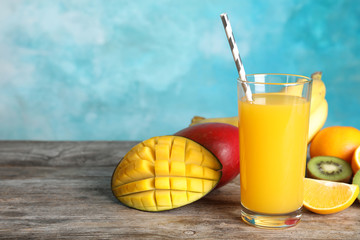 Glass with tasty mango juice and fresh fruits on table against color background. Space for text