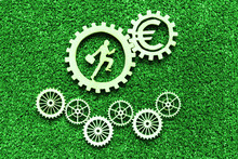 Gears, An Employee With A Suitcase, A Euro Sign On Green Background Of Artificial Grass. Business, Finance Concept.