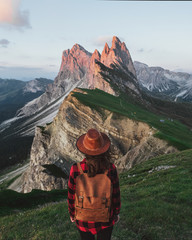 young traveler girl with backpack and hat standing on mountains at sunset.