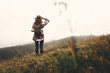 Stylish hipster girl in hat walking on top of mountains. Happy young woman with backpack exploring misty mountains. Travel and wanderlust concept. Amazing atmospheric moment