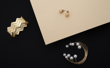 Wall Mural - Golden bracelets with pearls and zigzag shape cuff and pair of earrings on black and beige paper background