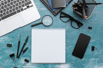 Opened notebook and other office equipment such as computer, pencil,  and glasses on wooden office desk.