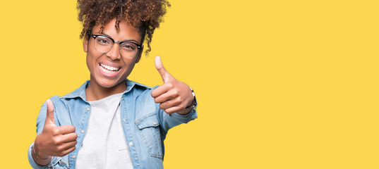 Beautiful young african american woman wearing glasses over isolated background approving doing positive gesture with hand, thumbs up smiling and happy for success. Looking at the camera