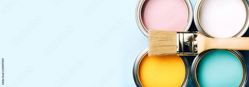 Banner of renovation concept. Brush with wooden handle on opened cans on blue pastel background. Yellow, white, pink, turquoise colors. Macro. - obrazy, fototapety, plakaty 