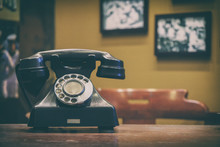 Old Style Telephone On Working Desk With Blurred Background Of Photo Hanging On Wall, Vintage Tone