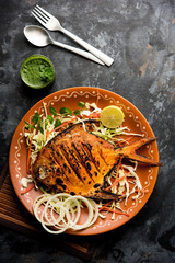 Tandoori Pomfret fish cooked in a clay oven and garnished with lemon , mint, cabbage and carrot salad. Selective focus