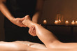 Close-up of male hands doing calf massage of female legs in a dark room with candles in the background. Cosmetology and spa treatments