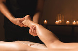Close-up of male hands doing calf massage of female legs in a dark room with candles in the background. Cosmetology and spa treatments