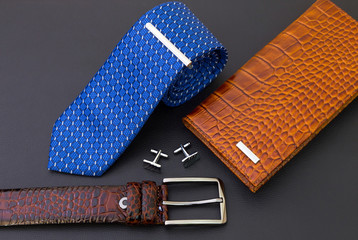 Sticker - Men's everyday accessories - blue tie with metal pin and cuff links, brown belt, wallet on black leather surface. Fashion concept