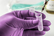 Scientist with green latex gloves manipulates vial and syringe in laboratory, conceptual image
