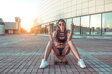 Beautiful girl sitting on a skateboard. The gesture of the hand shows middle finger. The concept of not trust, aggression. Long hair, black swimsuit. Confident look. Emotion leave me alone, go away.