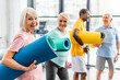 © LIGHTFIELD STUDIOS - selective focus of senior sportswoman holding fitness mat and her friends standing behind at gym
