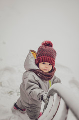 Canvas Print - Funny little child girl wearing in red hat, a scarf, and a warm winter suit with gloves having fun at winter day in beautiful winter park playing with snow