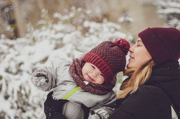 Wall Mural -  little child girl wearing in red hat, a scarf, and a warm winter suit. Happy loving family! Mother and child girl having fun, playing and laughing on snowy winter walk in nature. Frost winter season.