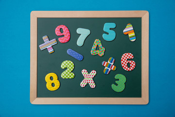 Wall Mural - Green chalkboard with wooden frame, colorful math operation signs and numbers, blue background