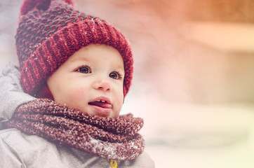 Wall Mural - Funny little child girl wearing in red hat, a scarf, and a warm winter suit with gloves having fun at winter day in beautiful winter park playing with snow