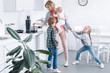 tired mother holding infant child and cooking while naughty children playing in kitchen