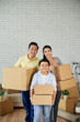 © DragonImages - Happy Vietnamese family of three holding cardboard boxes and smiling at camera