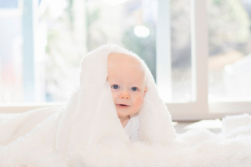 Beautiful 6 Month Baby Boy Dressed in White & Lying on Fluffly White Blanket Looking at Camera. Smiling & Happy