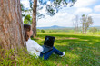 © sirastock - young woman sitting on green grass in park summer day while using laptop