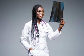 Wall Mural - African female nurse looking at a patients X-Ray wearing hospital scrubs isolated on gray