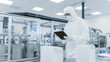 Quality Control Check: Scientist Using Digital Tablet Computer and wearing Protective Suit walks through Manufacturing Laboratory. Product Manufacturing: Pharmaceutics, Semiconductors, Biotechnology.