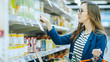 At the Supermarket: Beautiful Young Woman Browses through the Canned Goods Section of the Store. She Has Shopping Basket Full of Healthy Food Items.