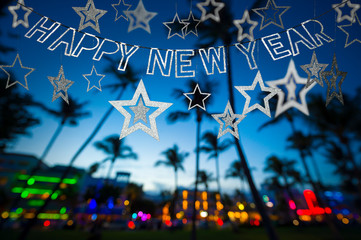 Happy New Year message hanging in glittery party bunting above tropical palm trees of the glowing neon lights of the skyline of Miami Beach, Florida, USA