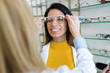 © nenetus - Young ophthalmologist putting on eyeglasses on smiling beautiful woman in optic shop.