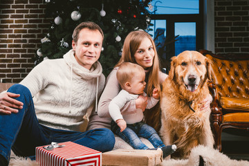 Wall Mural - theme Christmas and New Year family circle and domestic pet. Mom dad and child 1 year old Caucasian woman sitting on floor near Christmas tree with gifts and big dog breed labrador golden retriever