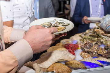 Sticker - A man delivers oysters on plates to visitors in iron gloves with a calculus.