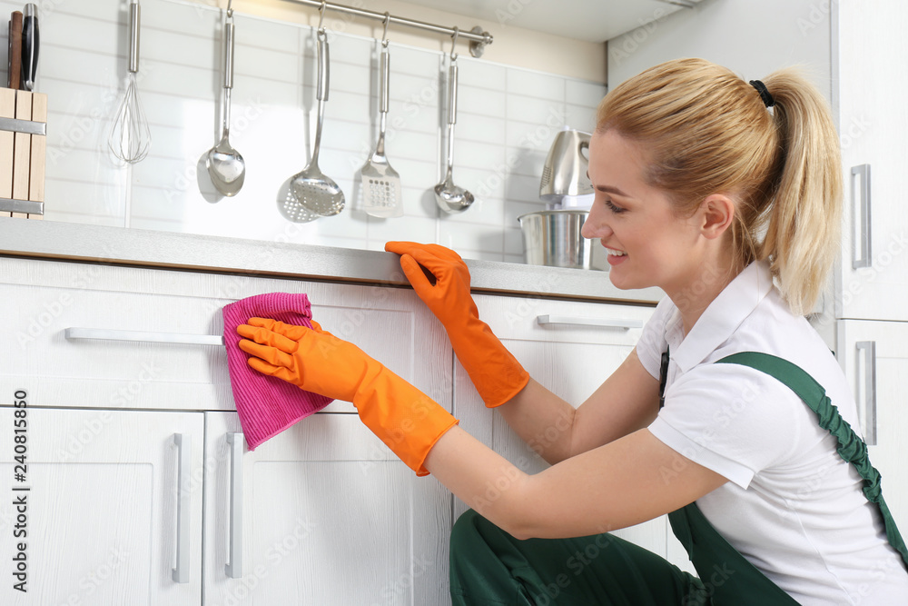 Female janitor cleaning cabinet with rag in kitchen - obrazy, fototapety, plakaty 